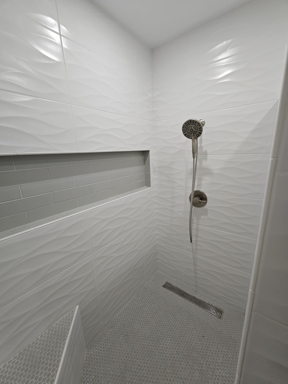 Custom white textured tile shower with 3D wave walls, built-in bench, niche and handheld shower head
